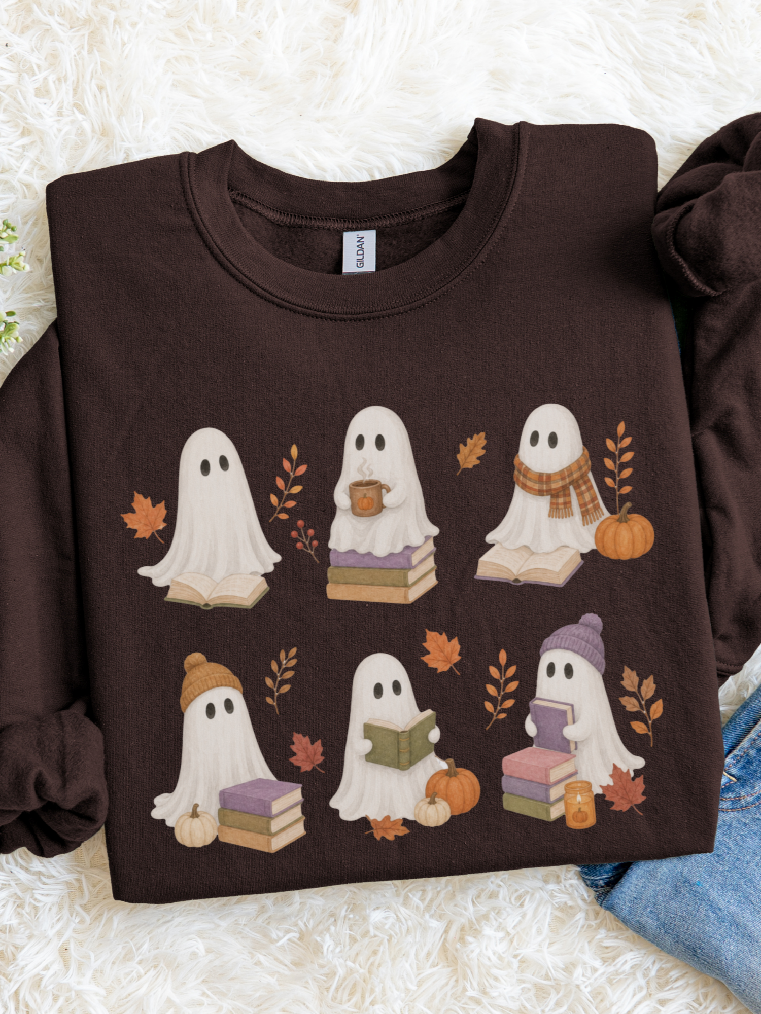 A dark chocolate long-sleeve crewneck sweatshirt featuring a cute cartoon ghost graphic with autumn details, laid flat on a white faux fur background.