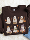 A dark chocolate long-sleeve crewneck sweatshirt featuring a cute cartoon ghost graphic with autumn details, laid flat on a white faux fur background.