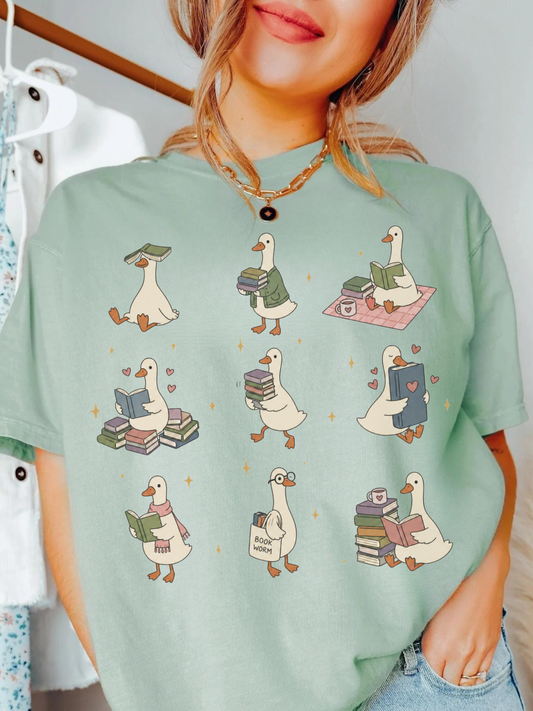 woman wearing bay comfort colors bookish goose reading shirt featuring cute ducks holding books reading and carrying stacks of novels