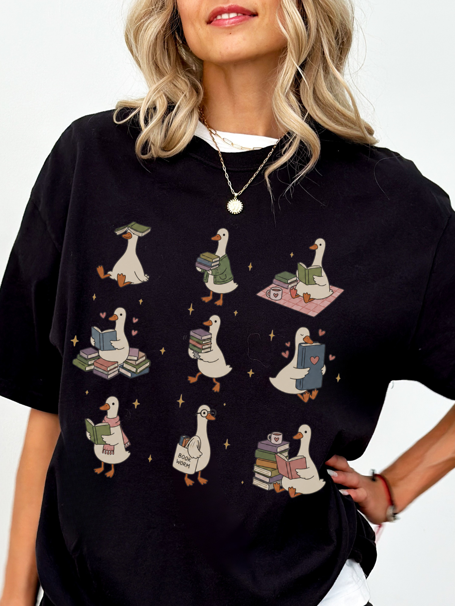 woman wearing black comfort colors bookish goose reading shirt with whimsical duck illustrations books hearts and cozy reading aesthetic