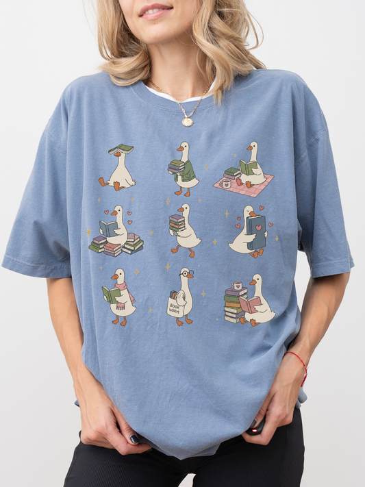 woman wearing blue jean comfort colors shirt with adorable reading geese illustration carrying books and cozy book lover artwork