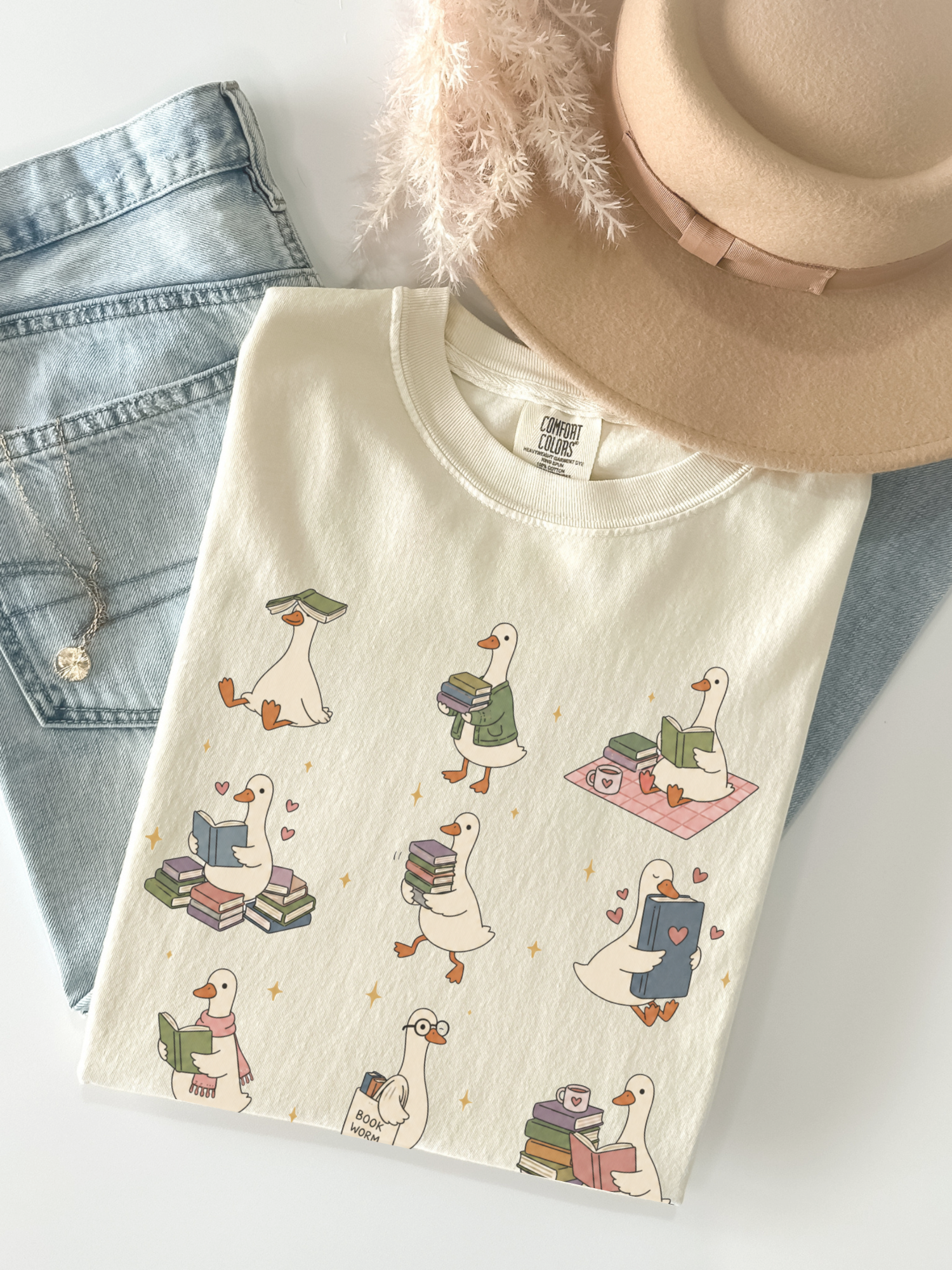ivory comfort colors bookish goose reading shirt flat lay with cute duck reader illustrations books coffee mug jeans and beige hat styling
