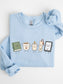 Gildan bookish sweatshirt with cute book, coffee mug, candle, bookmark and e-reader illustration in Light Blue