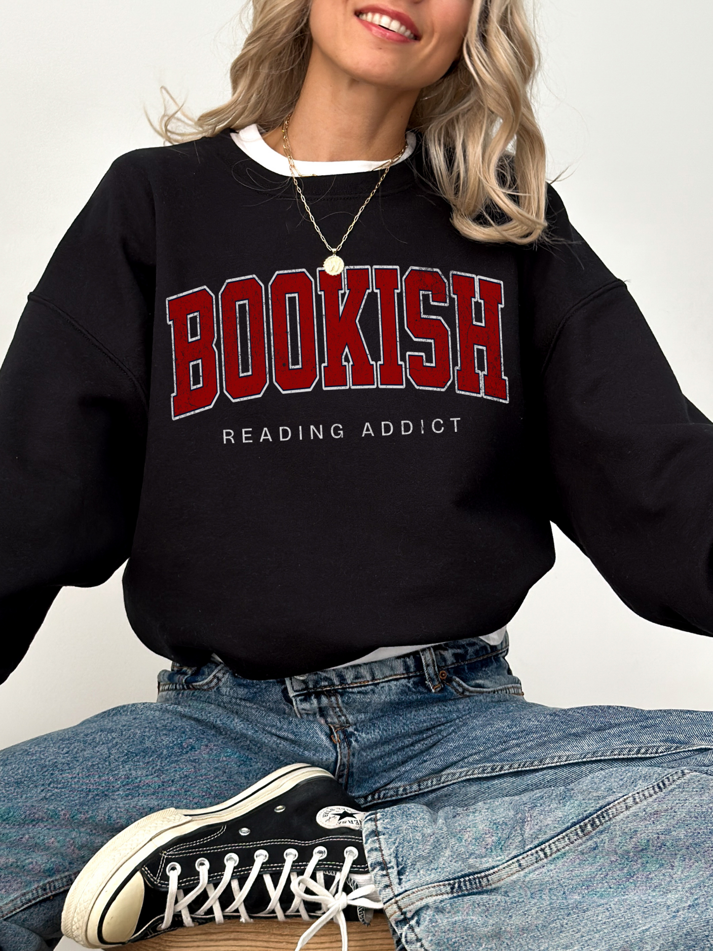 woman wearing black sweatshirt with red varsity "Bookish" text and "Reading Addict" tagline