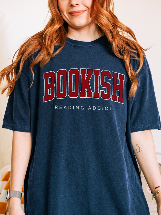 woman wearing navy Comfort Colors shirt that says Bookish Reading Addict in large red varsity print
