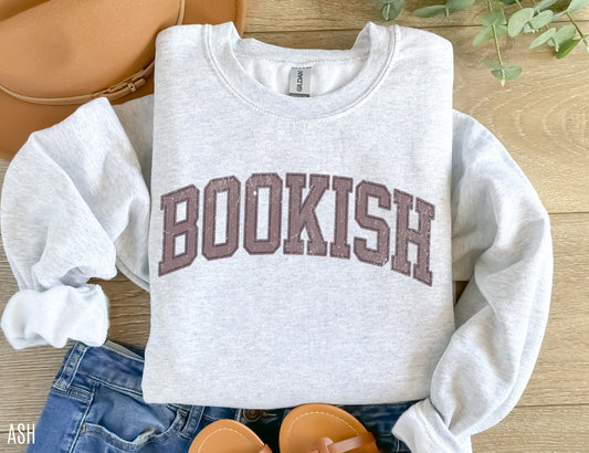folded ash grey sweatshirt with bookish text in varsity font, styled with jeans, sandals, and a tan hat