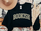 folded black sweatshirt with yellow bookish varsity text, styled with tan hat and neutral tones