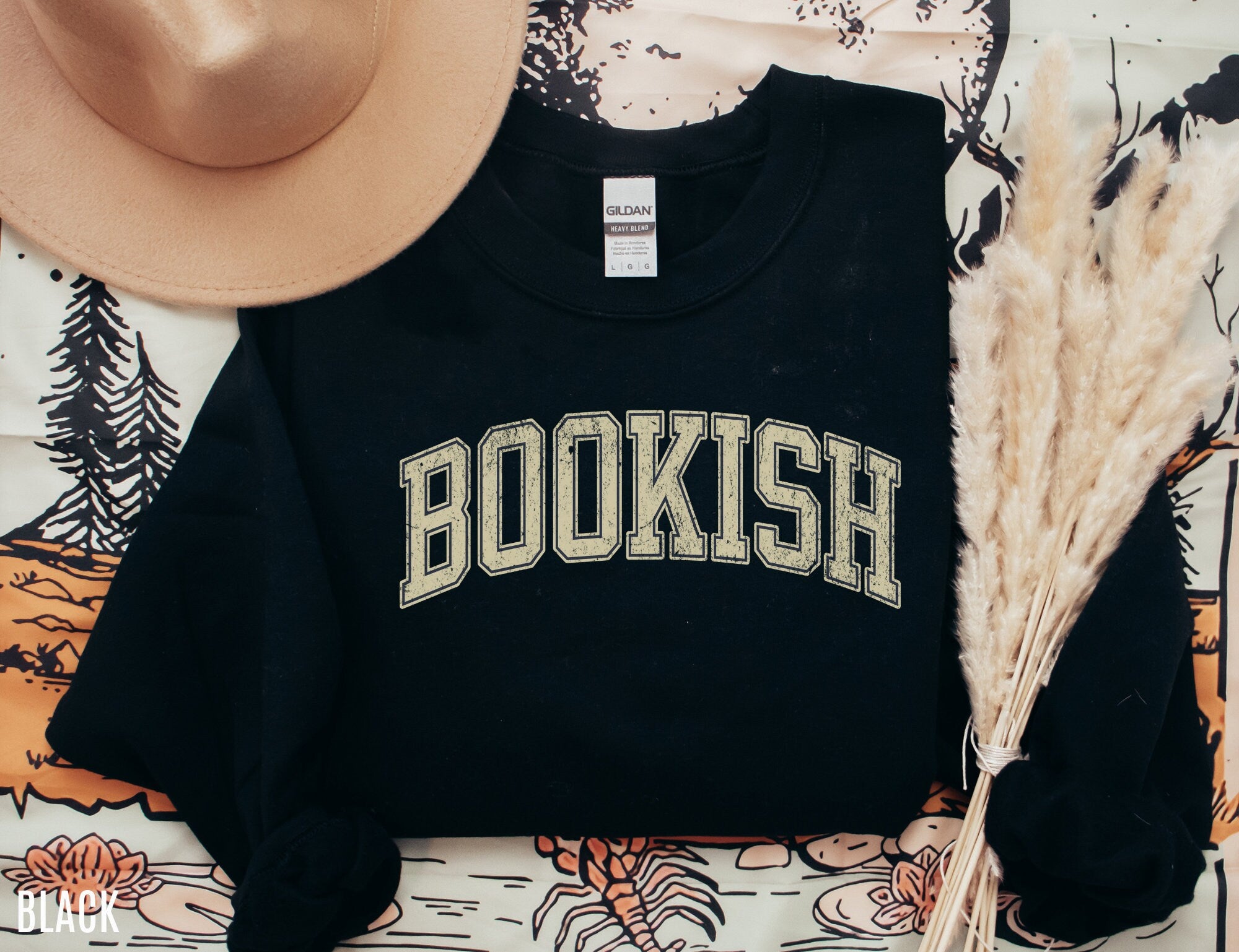 folded black sweatshirt with yellow bookish varsity text, styled with tan hat and neutral tones
