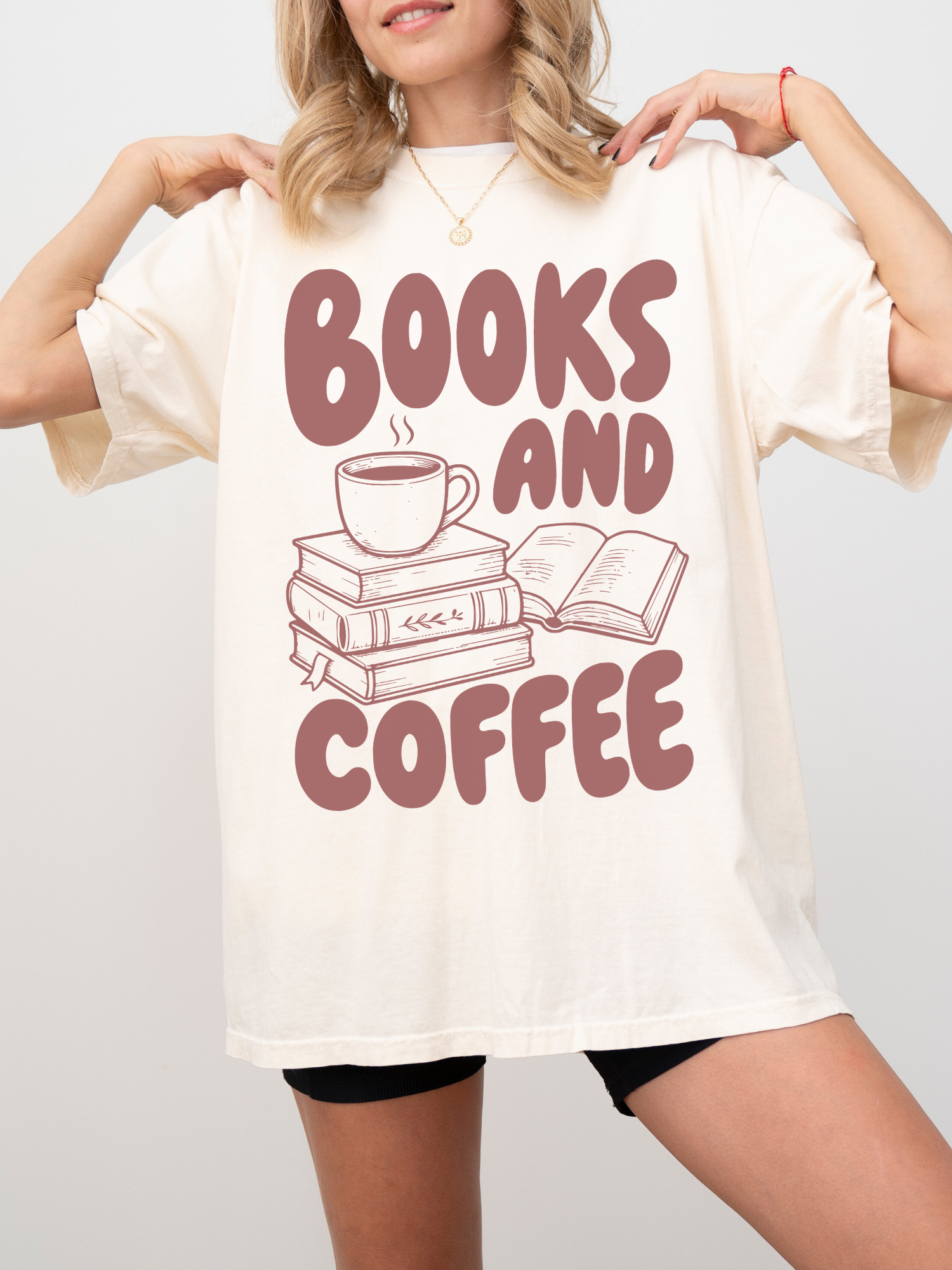 woman wearing an ivory Comfort Colors shirt featuring a books and coffee design with stacked books, open book, and coffee mug illustration, oversized book lover apparel for readers and coffee fans