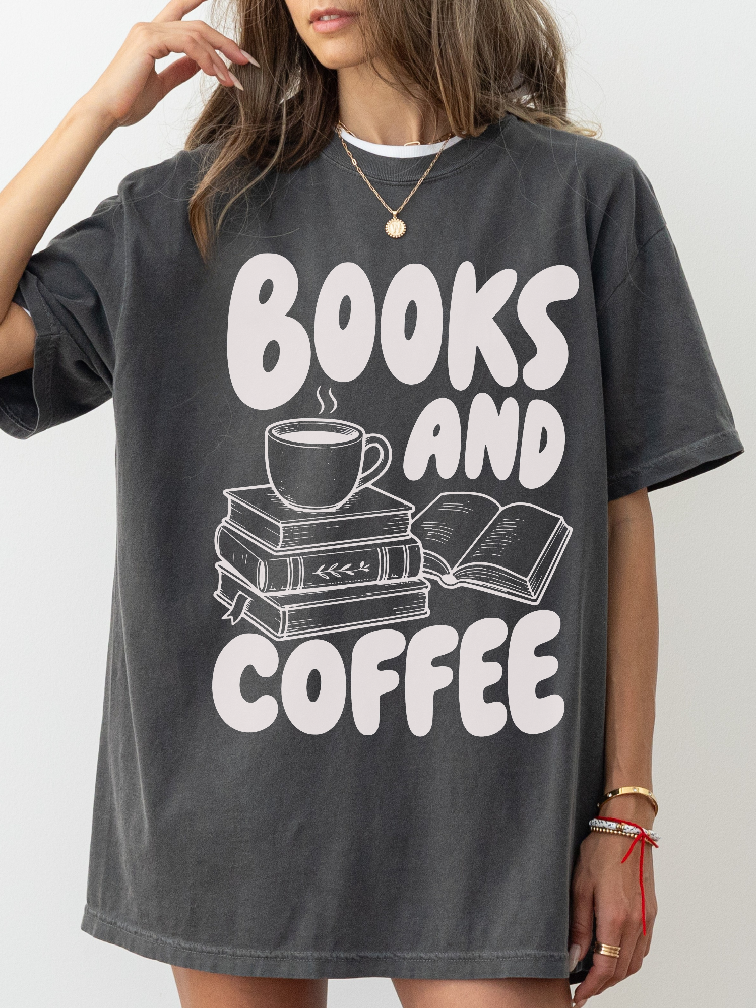 woman wearing a pepper Comfort Colors shirt featuring a books and coffee design with illustrated stacked books, open book, and coffee cup, cozy oversized bookworm shirt for readers and librarians