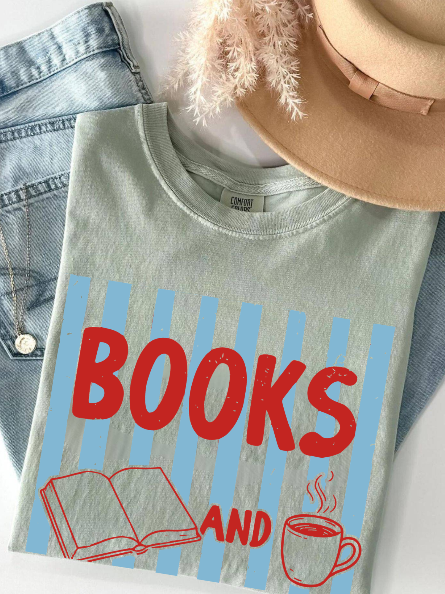 folded bay green comfort colors shirt with books and coffee graphic design styled with denim hat and jewelry for cozy book lover aesthetic