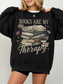 woman wearing oversized black sweatshirt with vintage floral books and coffee cup graphic that says books are my therapy