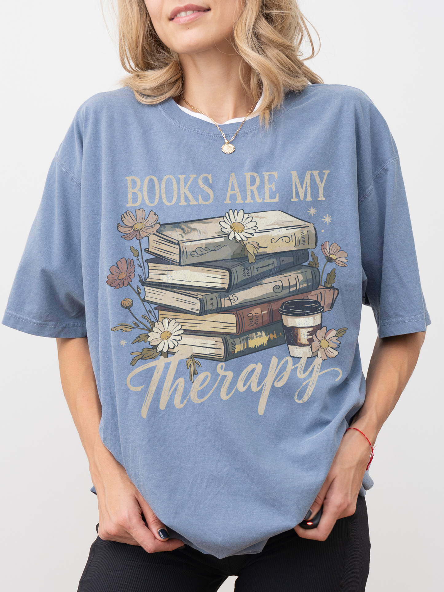 Woman wearing blue Books Are My Therapy Comfort Colors T-shirt with vintage book stack and floral illustration