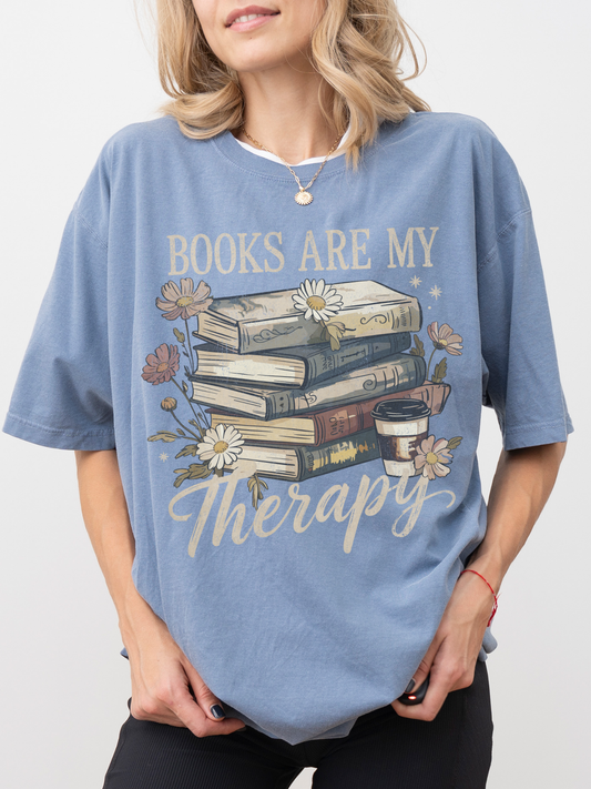Woman wearing blue Books Are My Therapy Comfort Colors T-shirt with vintage book stack and floral illustration