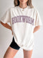 woman standing wearing an ivory comfort colors shirt that says "bookworm" in a college varsity style font