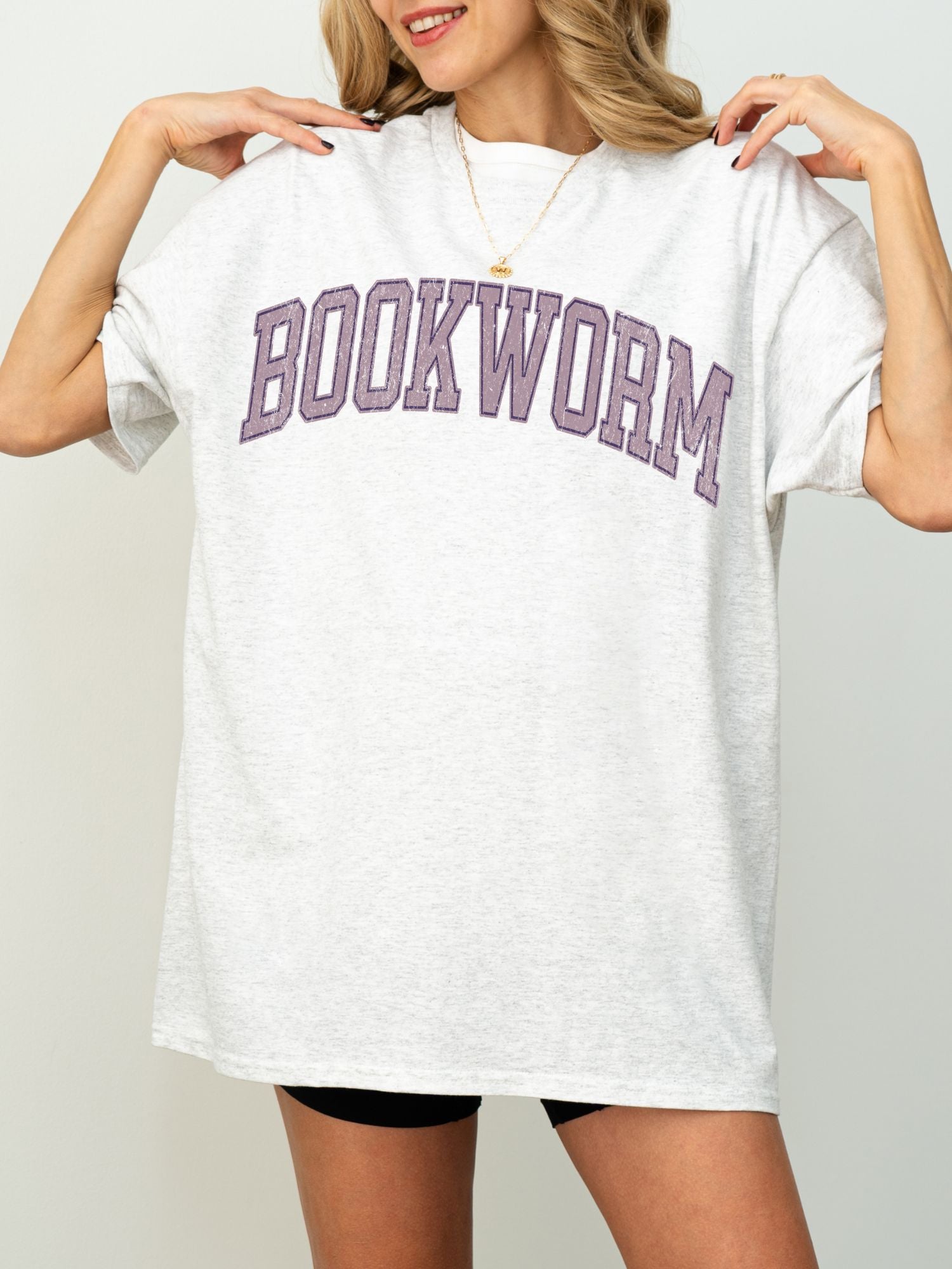 woman wearing a light grey t-shirt with purple varsity text that says bookworm in bold college font