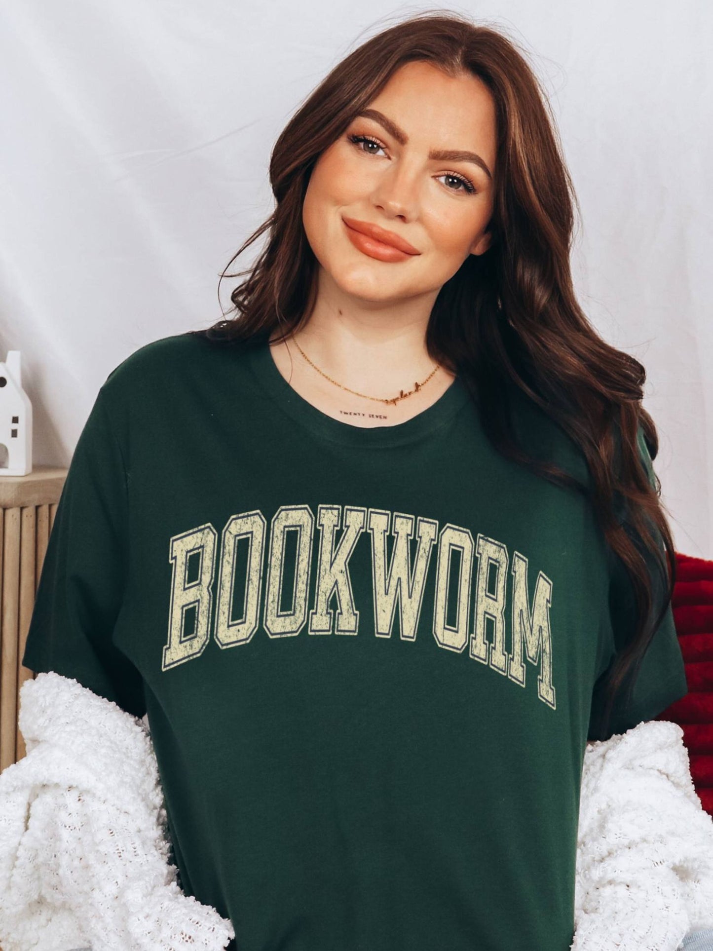 woman in forest green shirt that says bookworm in yellow varsity print while sitting indoors