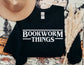 folded black sweatshirt with white bookworm things design laid out with pampas grass and hat