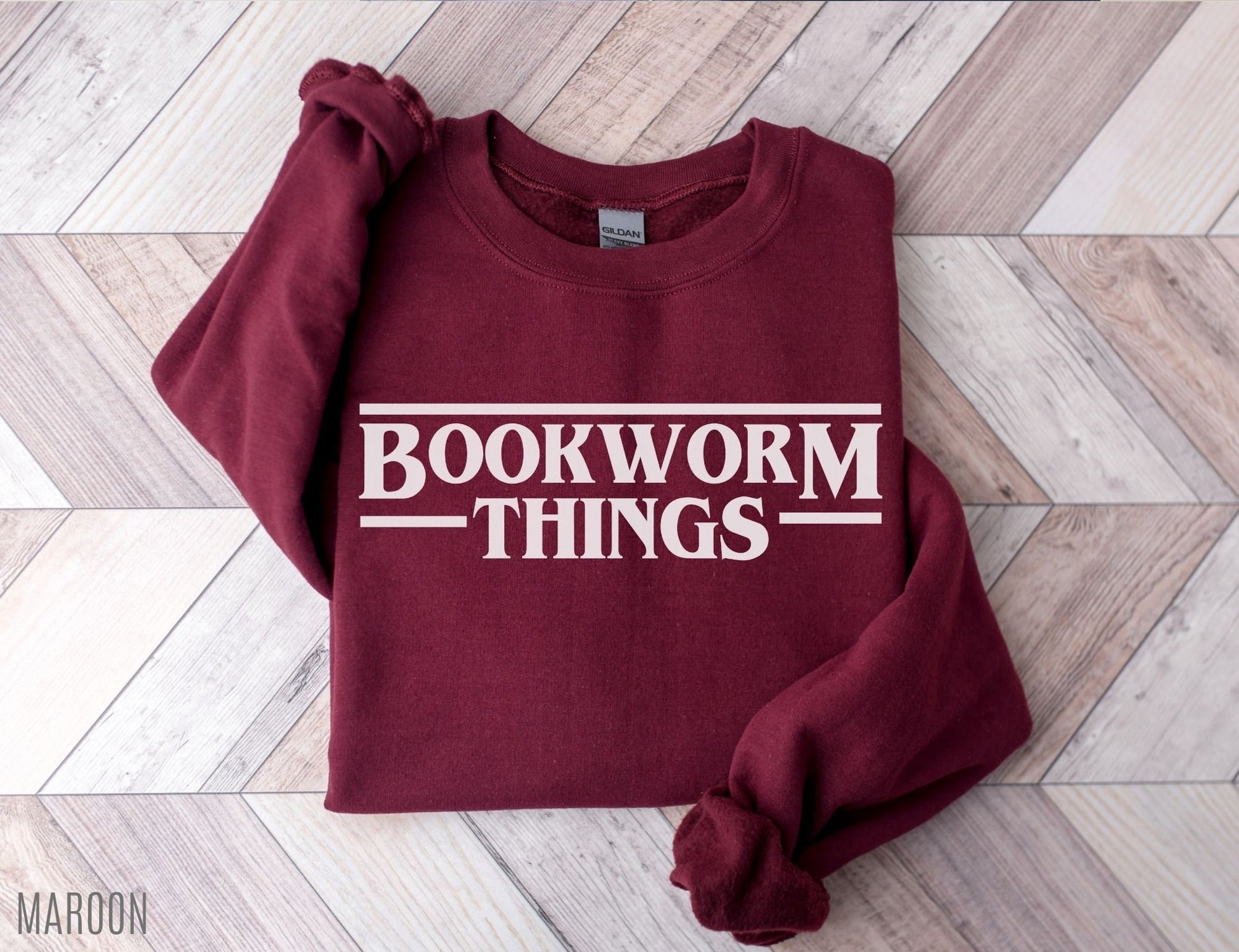 folded maroon sweatshirt with bold retro bookworm things text on herringbone background