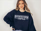 woman wearing navy sweatshirt that says bookworm things in a retro font 