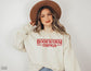 woman wearing sand sweatshirt that says bookworm things in red retro font with tan hat