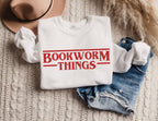 folded white sweatshirt with red bookworm things text styled with denim shorts and hat