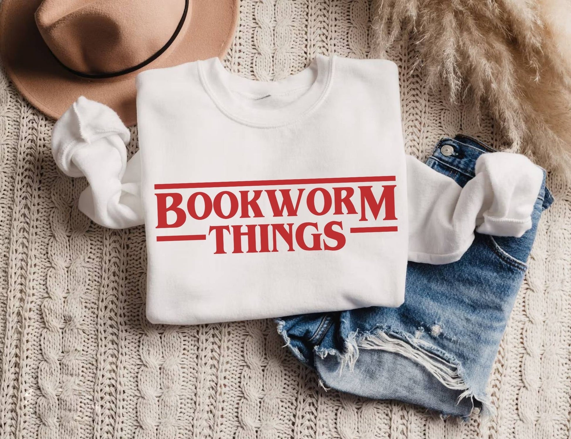 folded white sweatshirt with red bookworm things text styled with denim shorts and hat