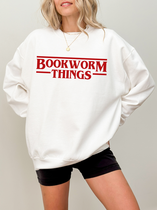 woman wearing oversized white sweatshirt that says bookworm things in red font with black biker shorts