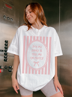 Woman wearing a cream oversized t shirt with pink striped vintage frame graphic and text buy me books and tell me I’m pretty styled casually indoors