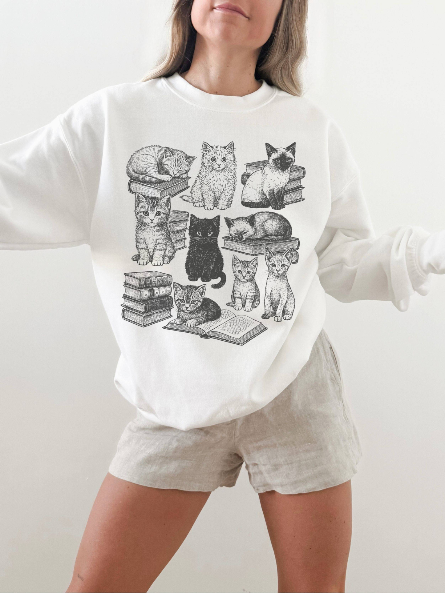 woman wearing white sweatshirt with vintage cat illustrations sitting and sleeping on books