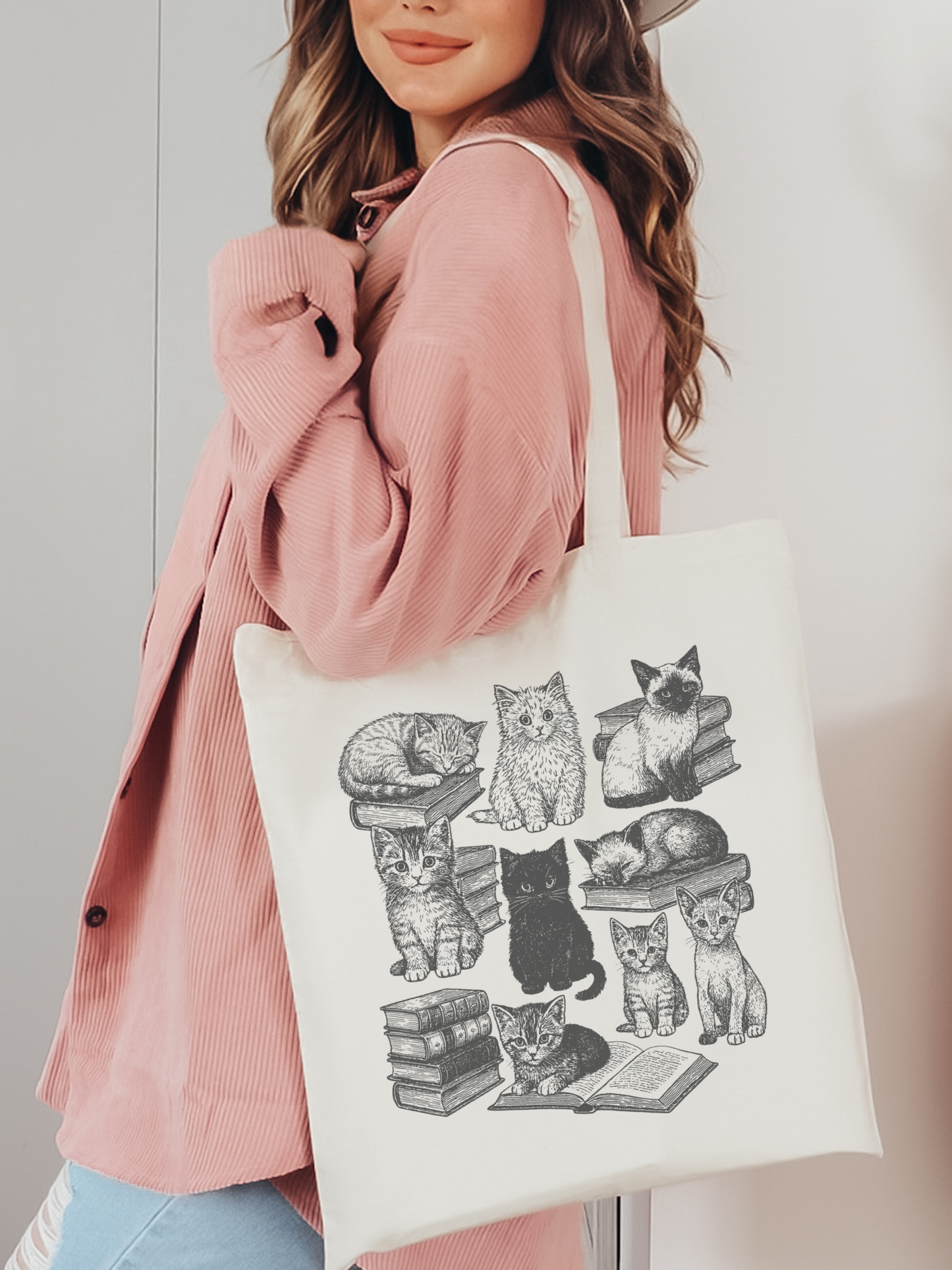 woman holding canvas tote bag with cute black and white cat and book print, styled with pink corduroy jacket and hat