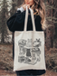 cozy reading tote bag with vintage cat illustration, modeled in forest setting with black coat