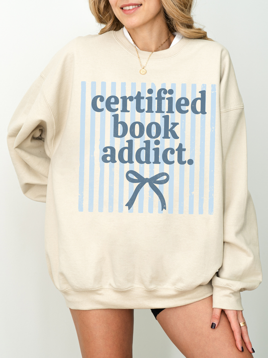 close up of certified book addict graphic on sand sweatshirt with blue stripes and minimalist bow design for book lovers
