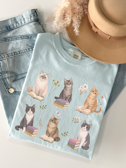 Flat lay of chambray Comfort Colors t shirt featuring cute cats with books and floral details styled with jeans necklace and neutral beige hat