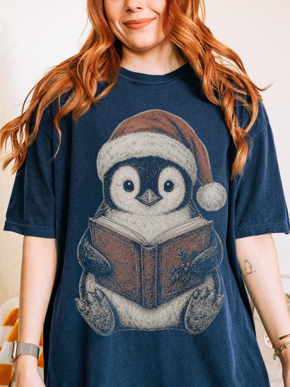 Model wearing a True Navy Comfort Colors bookish shirt featuring a festive penguin wearing a Santa hat and reading a Christmas book