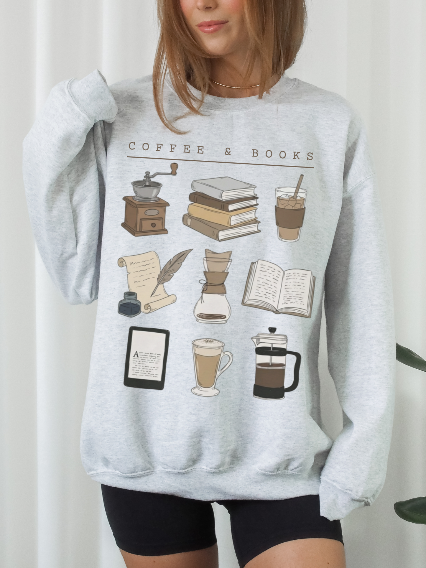 woman wearing light gray coffee and books sweatshirt featuring latte, kindle, french press and book stack illustrations