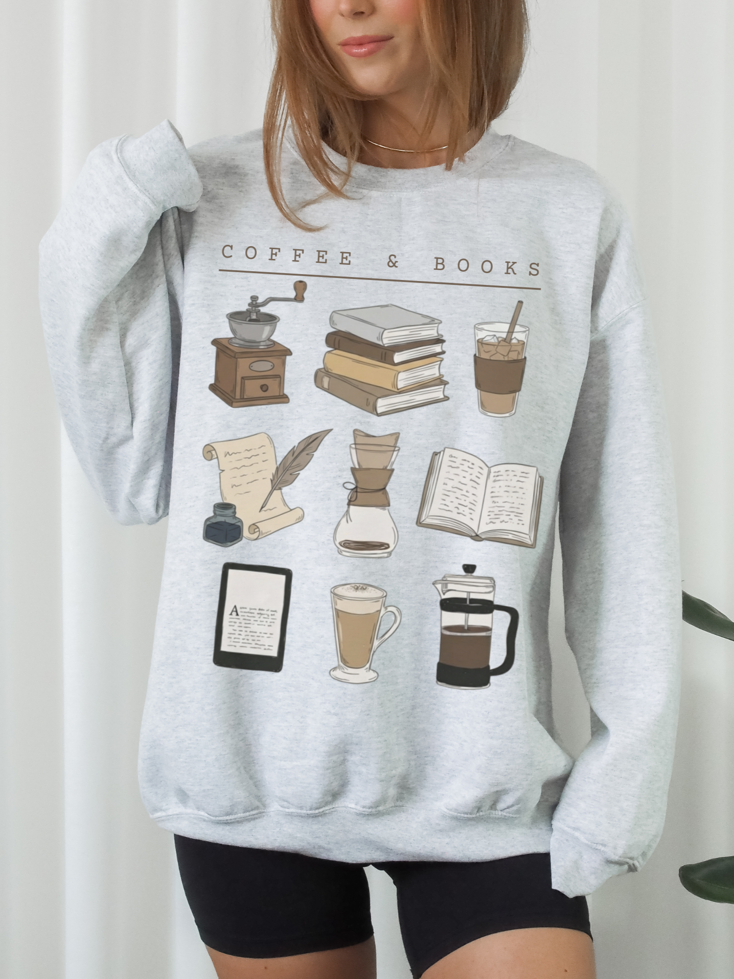 woman wearing light gray coffee and books sweatshirt featuring latte, kindle, french press and book stack illustrations