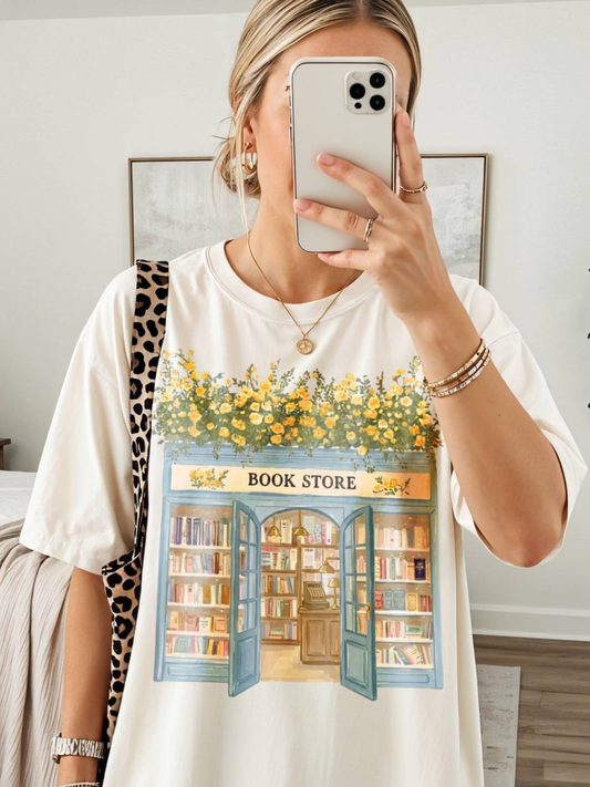 Woman taking a mirror selfie wearing a ivory t shirt with a cozy bookstore design featuring floral accents, open doors, and bookshelves paired with a leopard print bag in a modern bedroom
