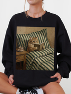 Black sweatshirt featuring a cozy cat reading a book illustration, styled on a seated model wearing casual sneakers. The relaxed lifestyle pose highlights a comfortable and laid back reading vibe, making it perfect for book lovers, cozy outfit inspiration, and fans of cat themed apparel.