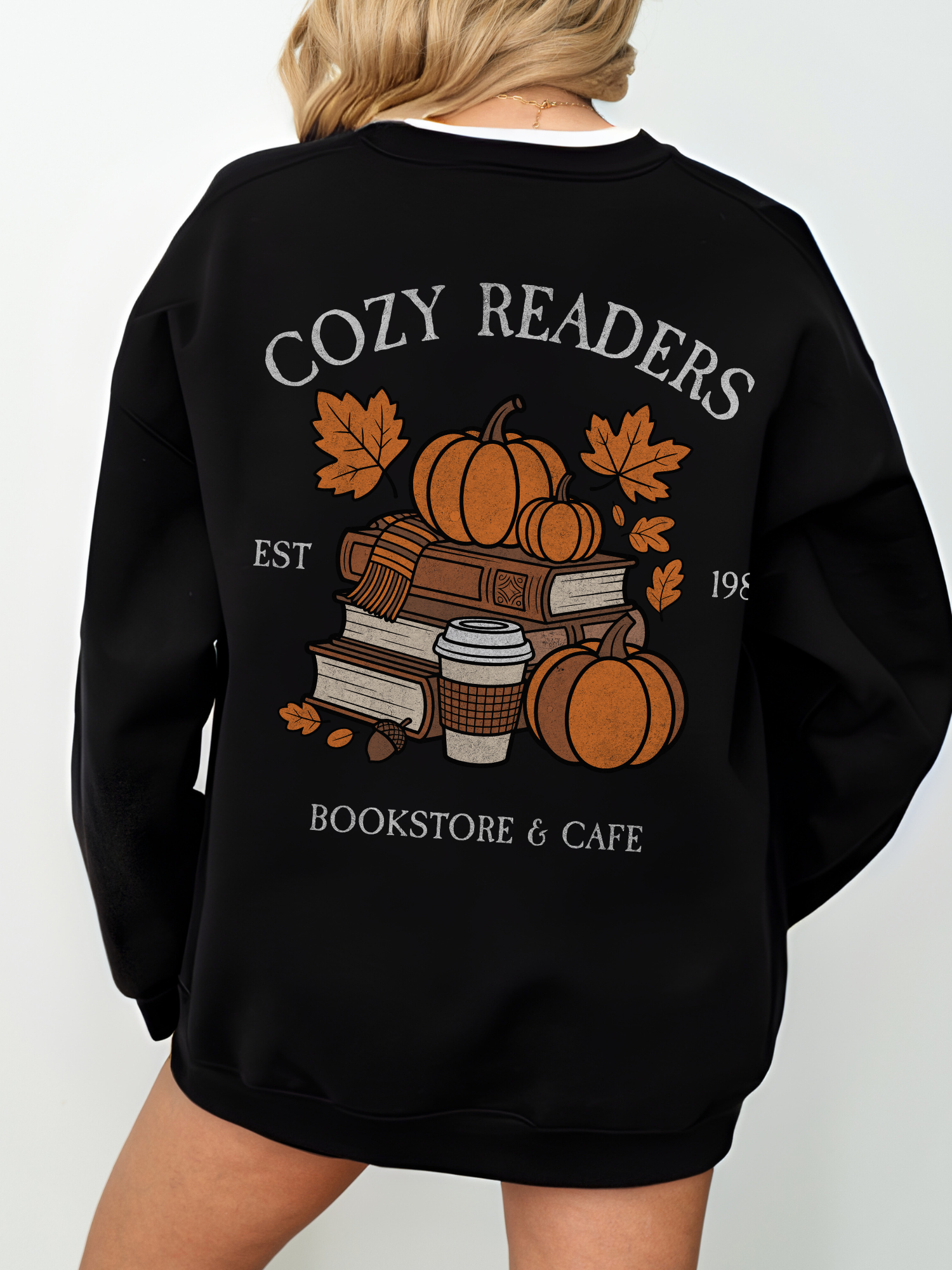 Back of black Cozy Readers crewneck showing large graphic of pumpkins, books, takeaway coffee cup, and leaves. Text reads Cozy Readers Bookstore and Cafe EST 1983.