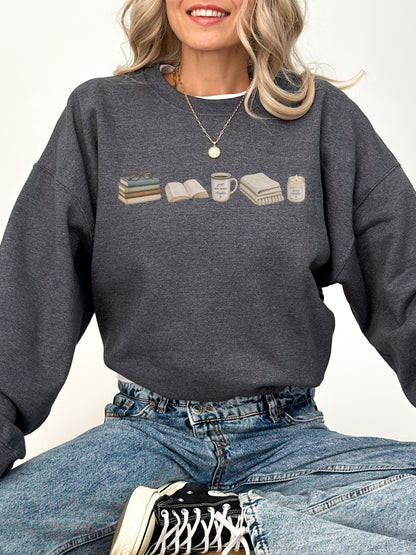 Woman wearing a dark heather Gildan book lover sweatshirt with books, coffee mug, blanket and candle design