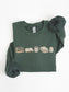 Folded forest green Gildan reading sweatshirt with books, coffee mug, cozy blanket and candle design