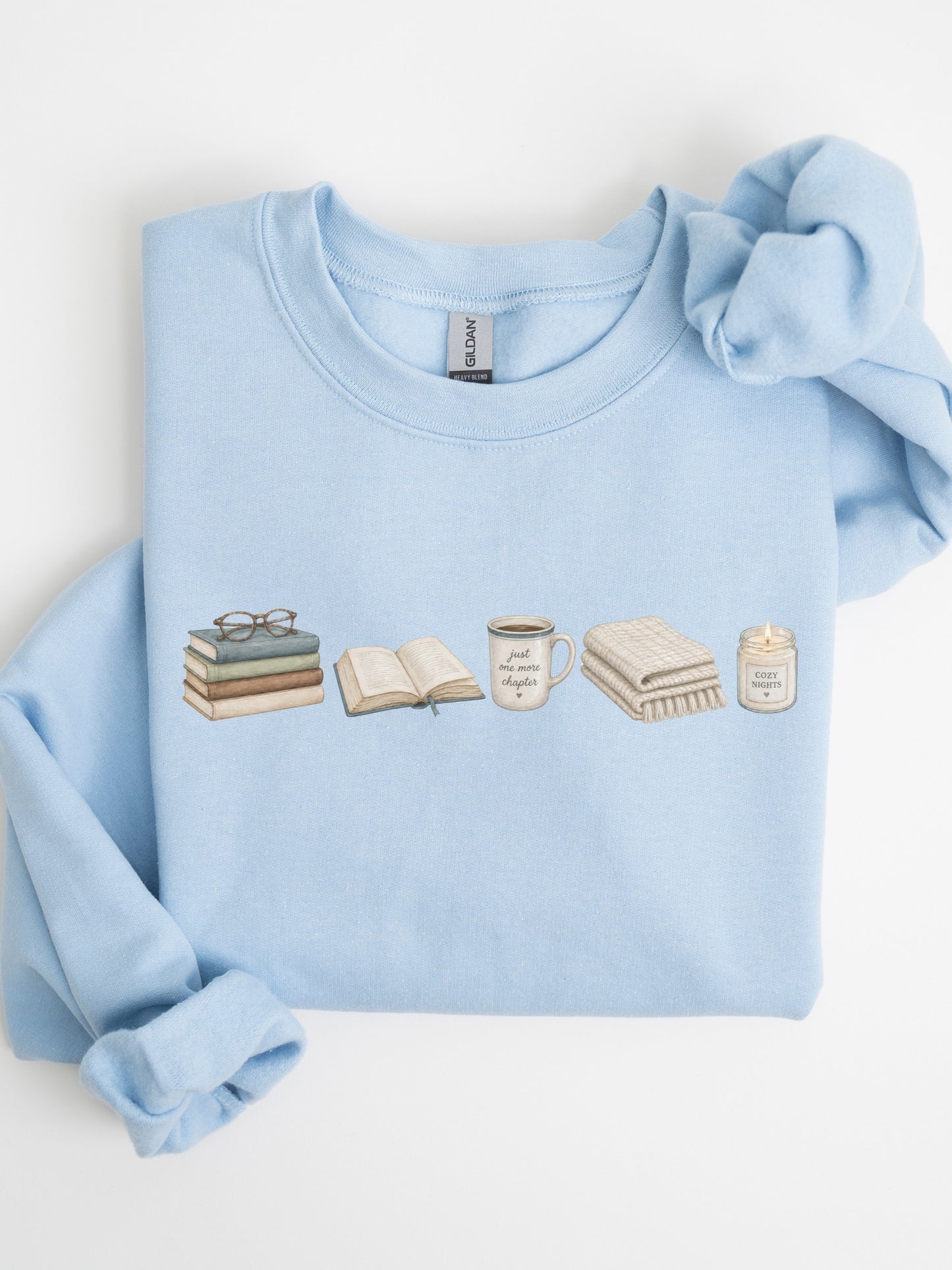 Folded light blue Gildan sweatshirt with books, Just One More Chapter coffee mug, blanket and cozy candle design