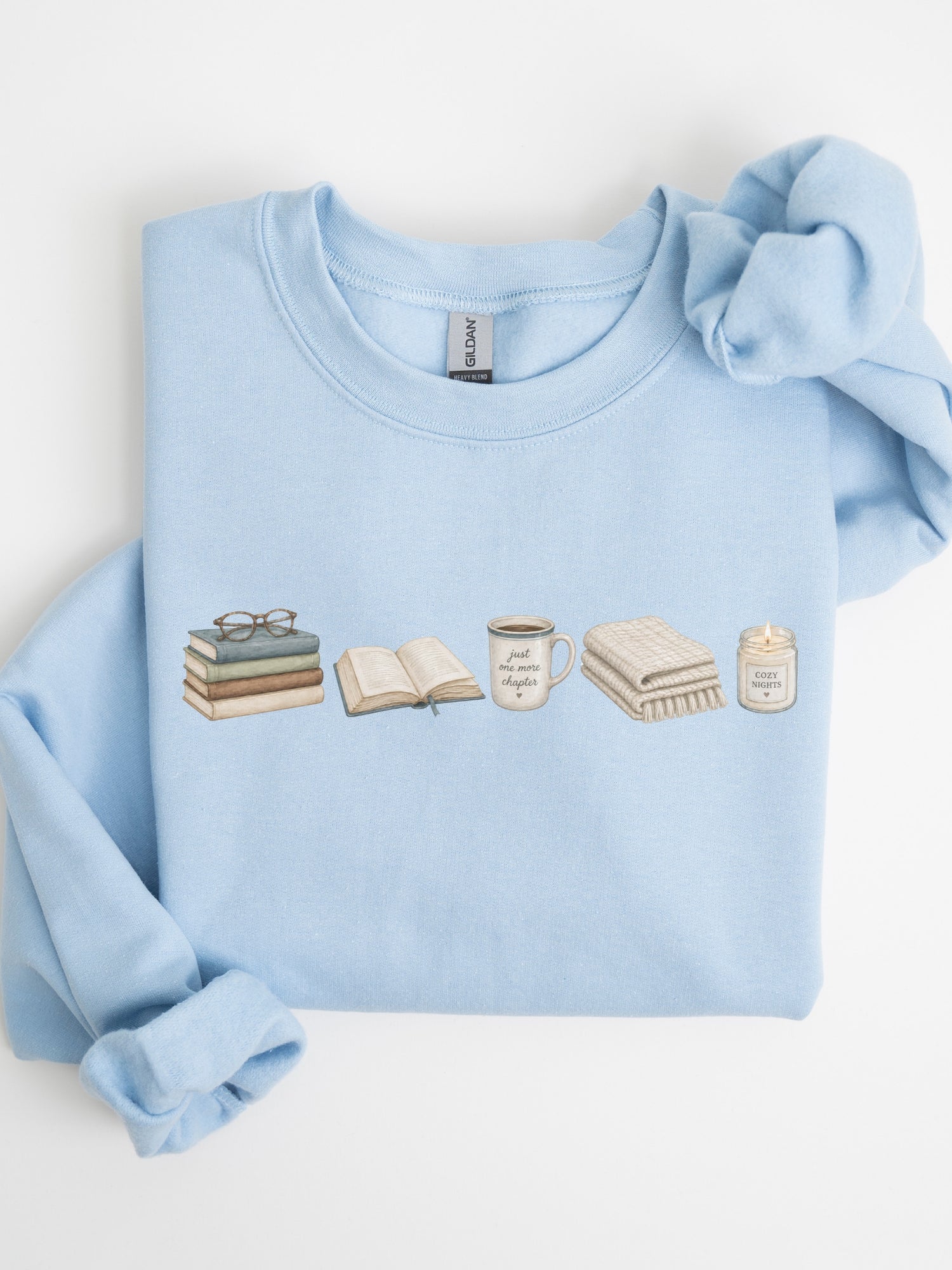 Folded light blue Gildan sweatshirt with books, Just One More Chapter coffee mug, blanket and cozy candle design