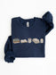 Folded navy Gildan book lover sweatshirt featuring books, Just One More Chapter mug, blanket and candle design