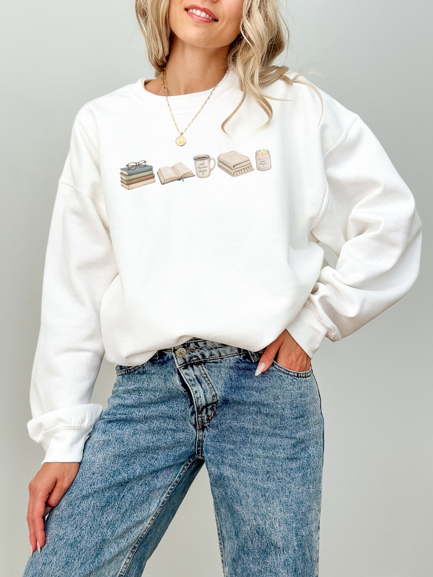 Woman wearing a white Gildan reading sweatshirt featuring books, Just One More Chapter mug, blanket and candle