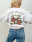 girl showing the back of an ash grey sweatshirt with a large cozy reader holiday cafe graphic and books