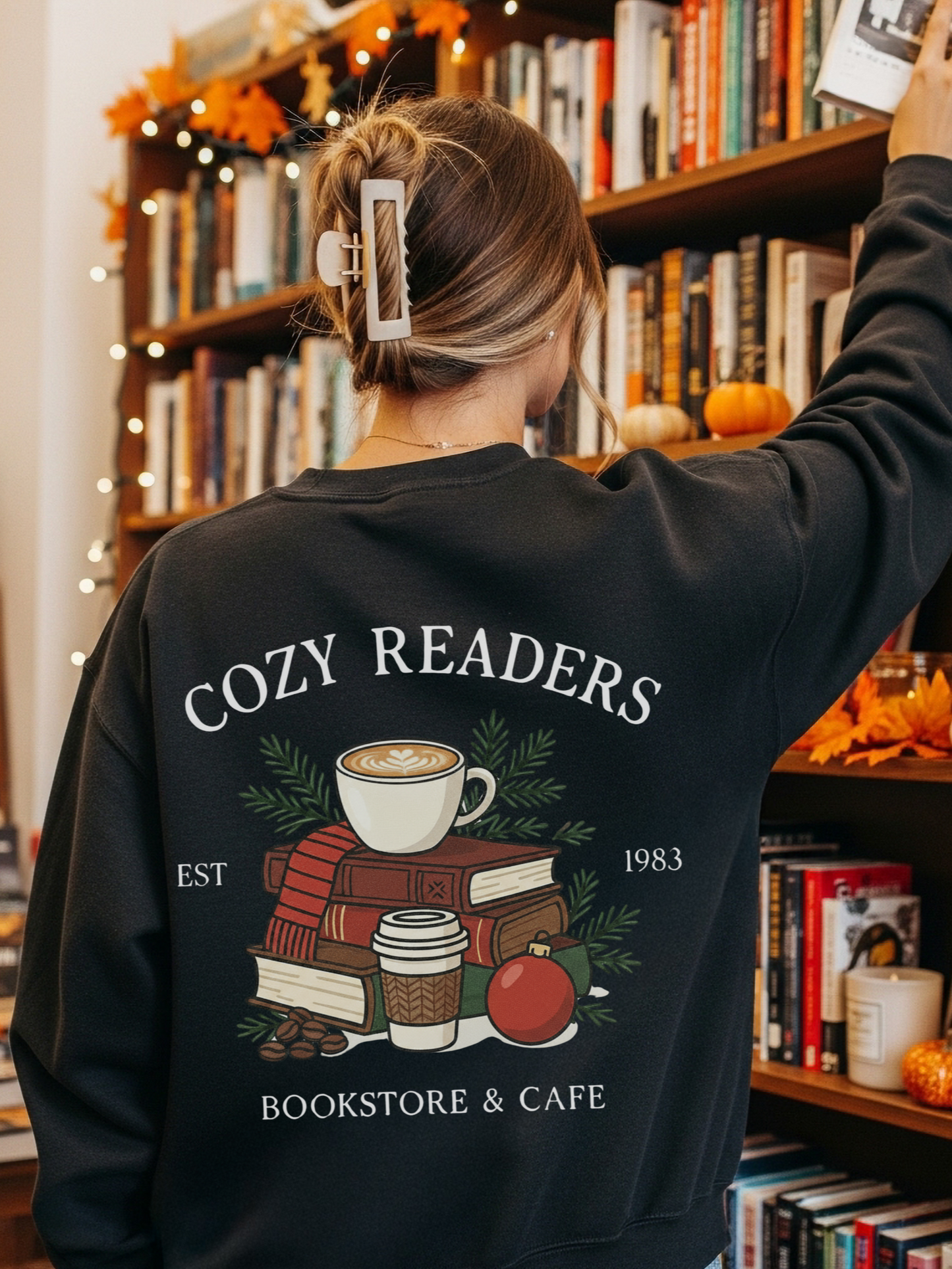 girl standing in a holiday-decorated bookstore wearing a black sweatshirt with a cozy reader holiday graphic on the back