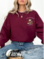 girl sitting cross-legged wearing a maroon sweatshirt with a cozy reader coffee shop logo on the front chest