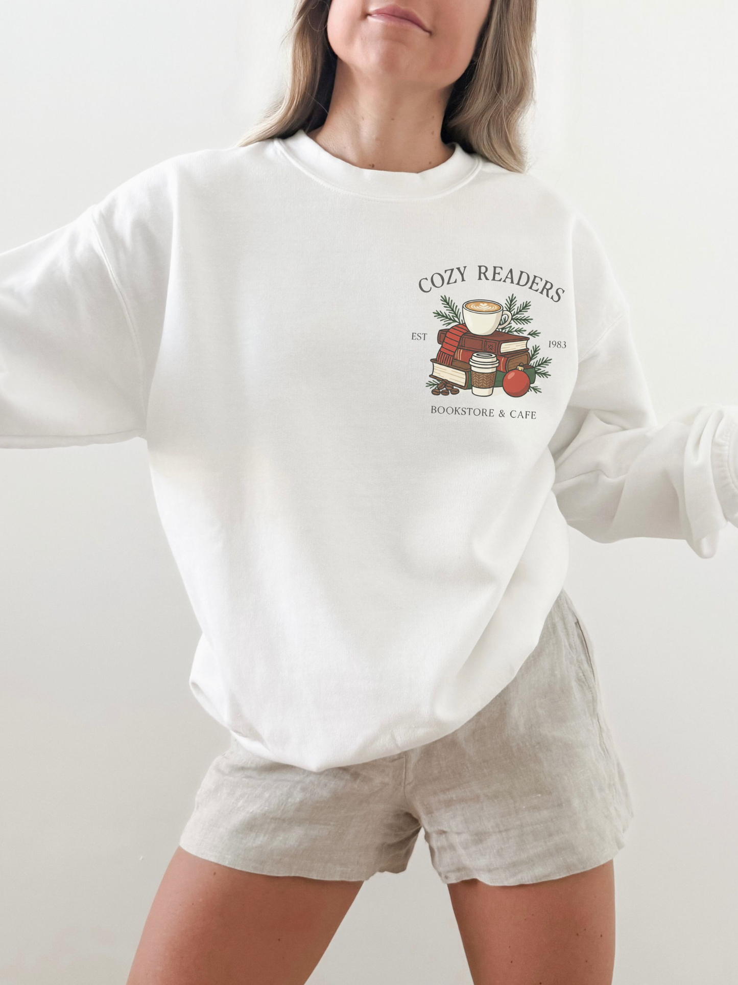girl standing wearing a white sweatshirt with a small cozy readers coffee shop graphic on the front chest
